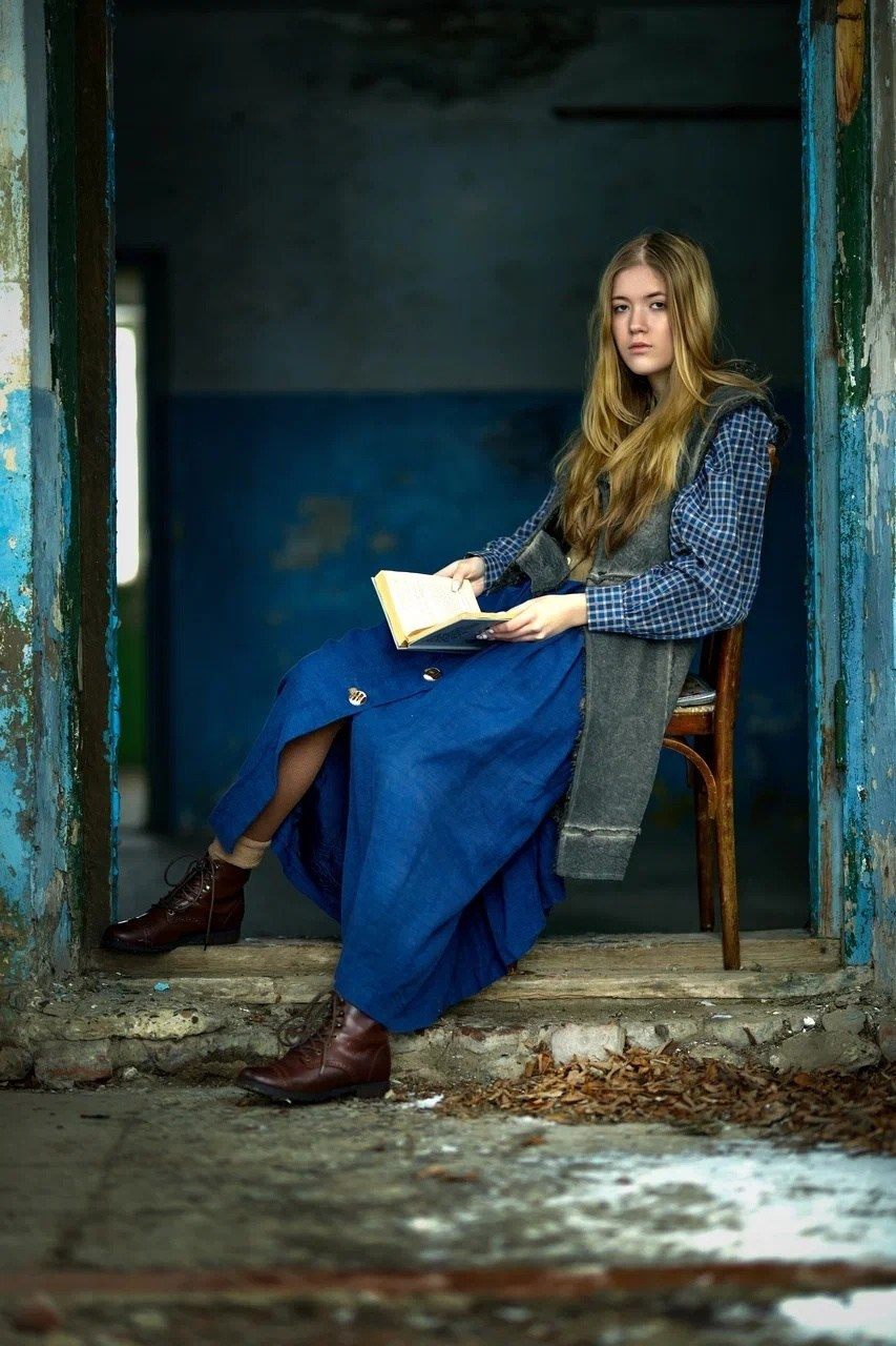 Девочка сидит на входе в заброшенный дом и читает книгу