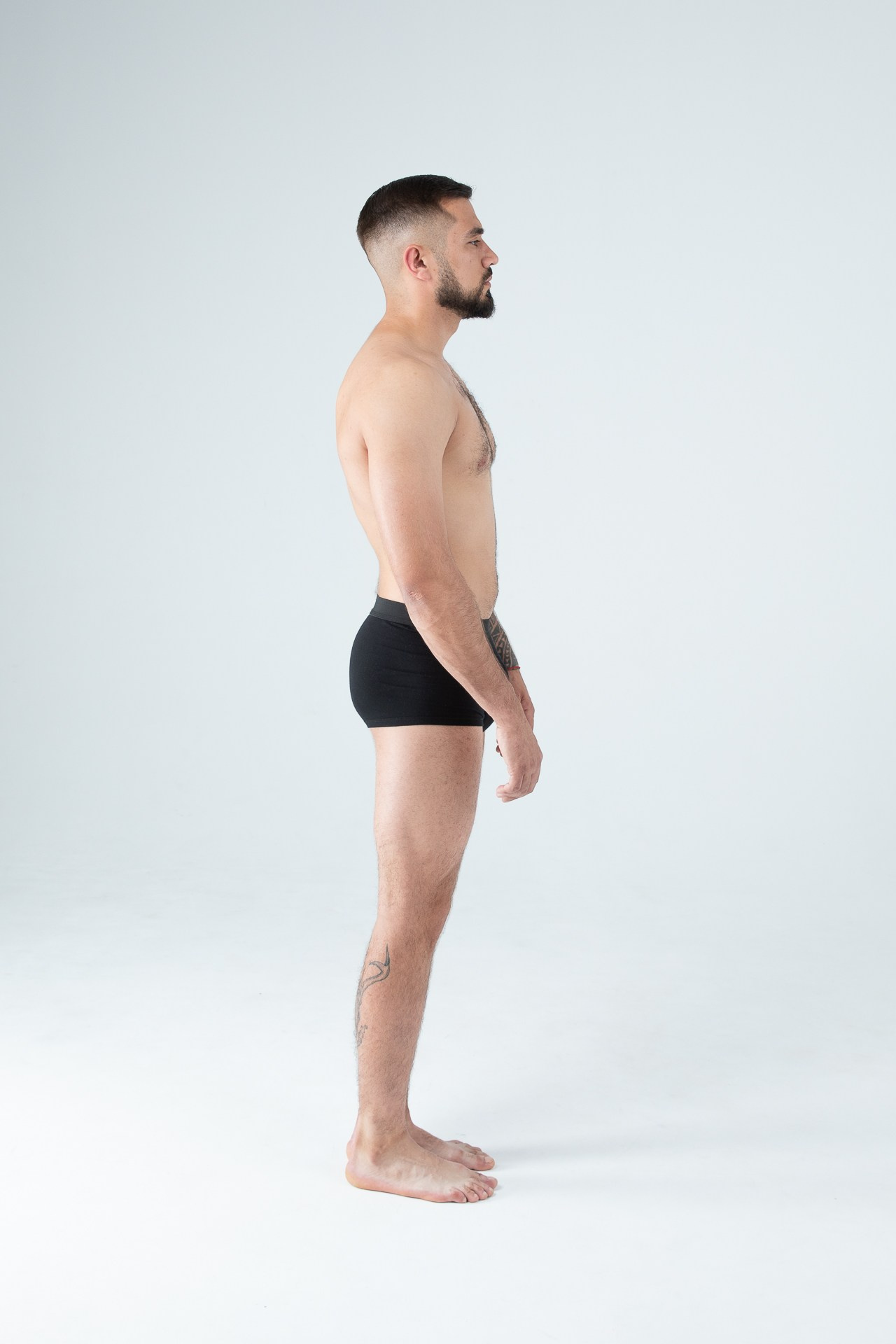 Мужчина модель с бородой с татуировками в черных трусах