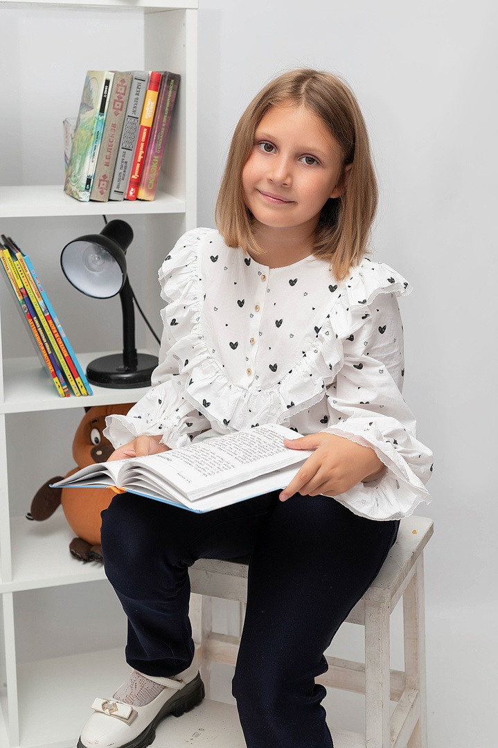 Милая девочка сидя на стуле фотографируется на обложку.