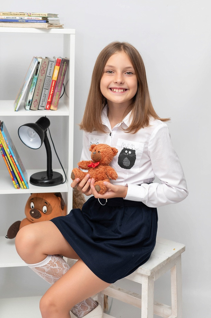 Красивая девочка с медвежонком позирует фотографу на стуле.