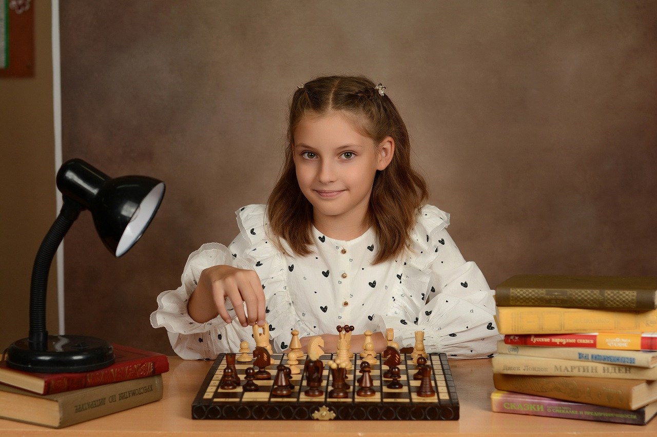 Фото красивой четвероклашки за игрой в шахматы.