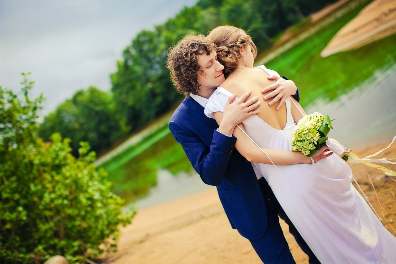 жених обнимает за спину невесту на фоне лесного озера и зеленого леса