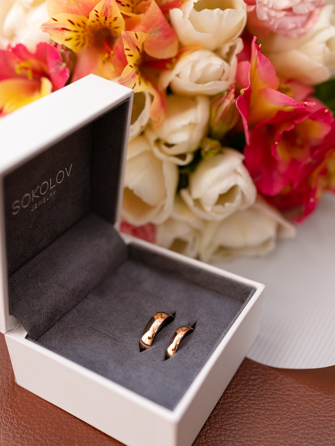 Свадебные кольца лежат в коробочке на фоне свадебного букета