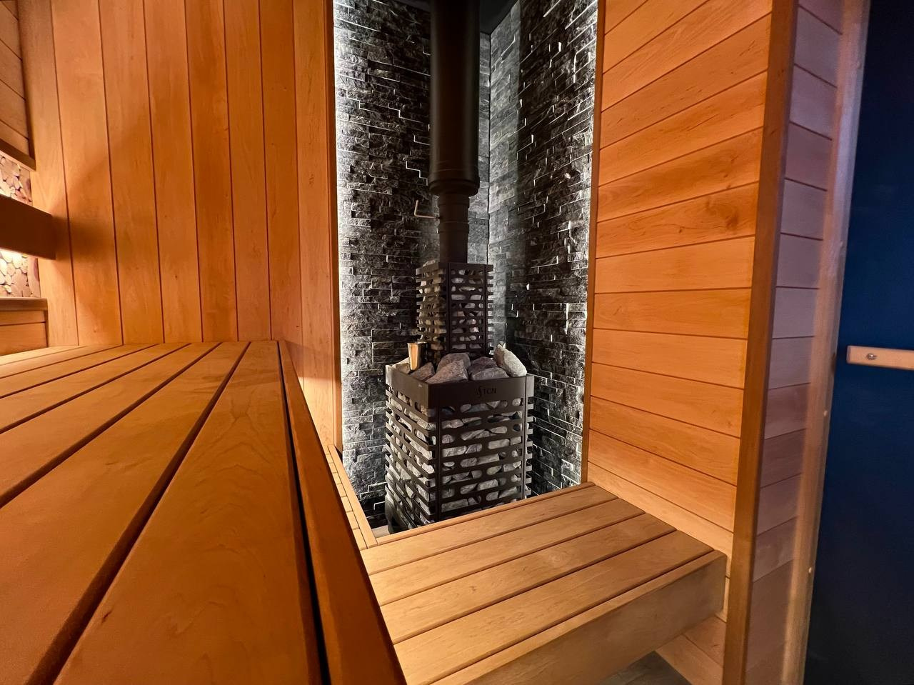 Семейная баня в Рощино из ольхи с можжевеловым панно, яркой печной зоной, закарнизной подсветкой и печью от производителя Aston. SaunaTopMasters