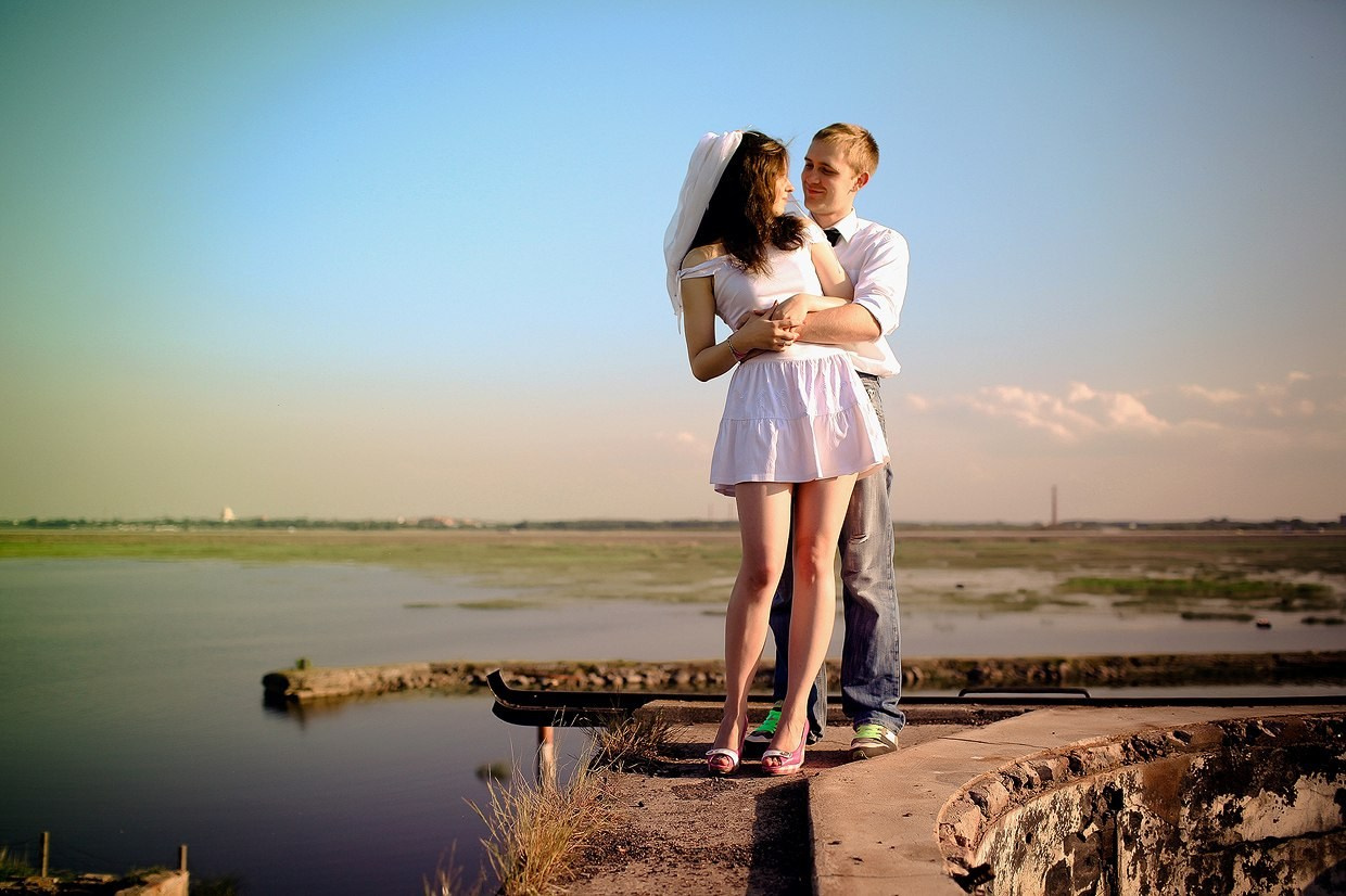 жених обнимает невесту в коротком платье на стене форта в финском заливе