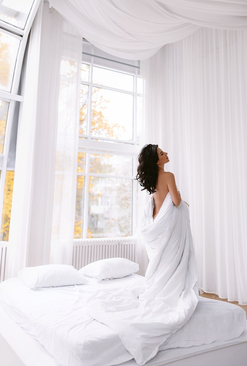 Силуэт женщины в белом покрывале у большого окна — нежный свет и спокойная атмосфера