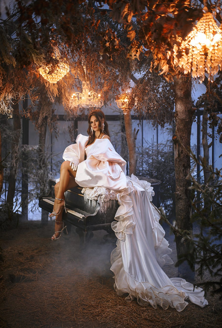 Дама в белом платье с огненными эффектами сидит на рояле