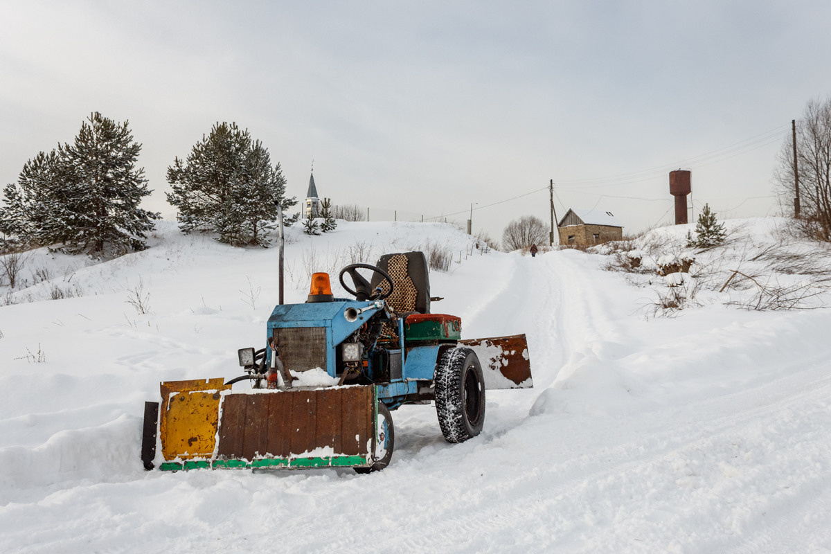 Разноцветный маленький трактор на снежной дороге в деревне.