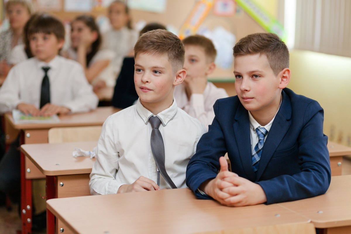 Два мальчика школьника сидят за парты в своей школе