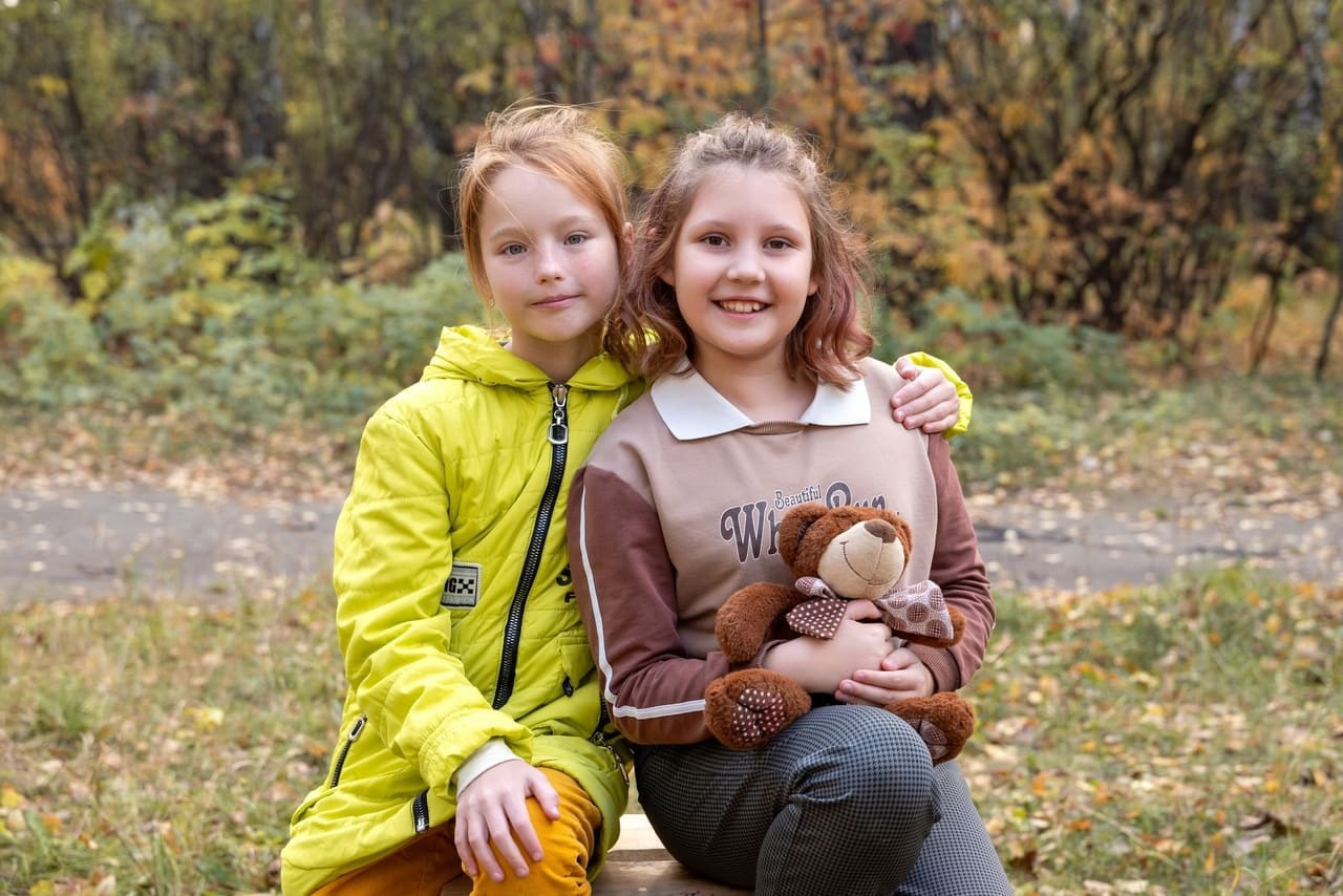 Две подружки одноклассницы позируют фотографу в осеннем лесу.