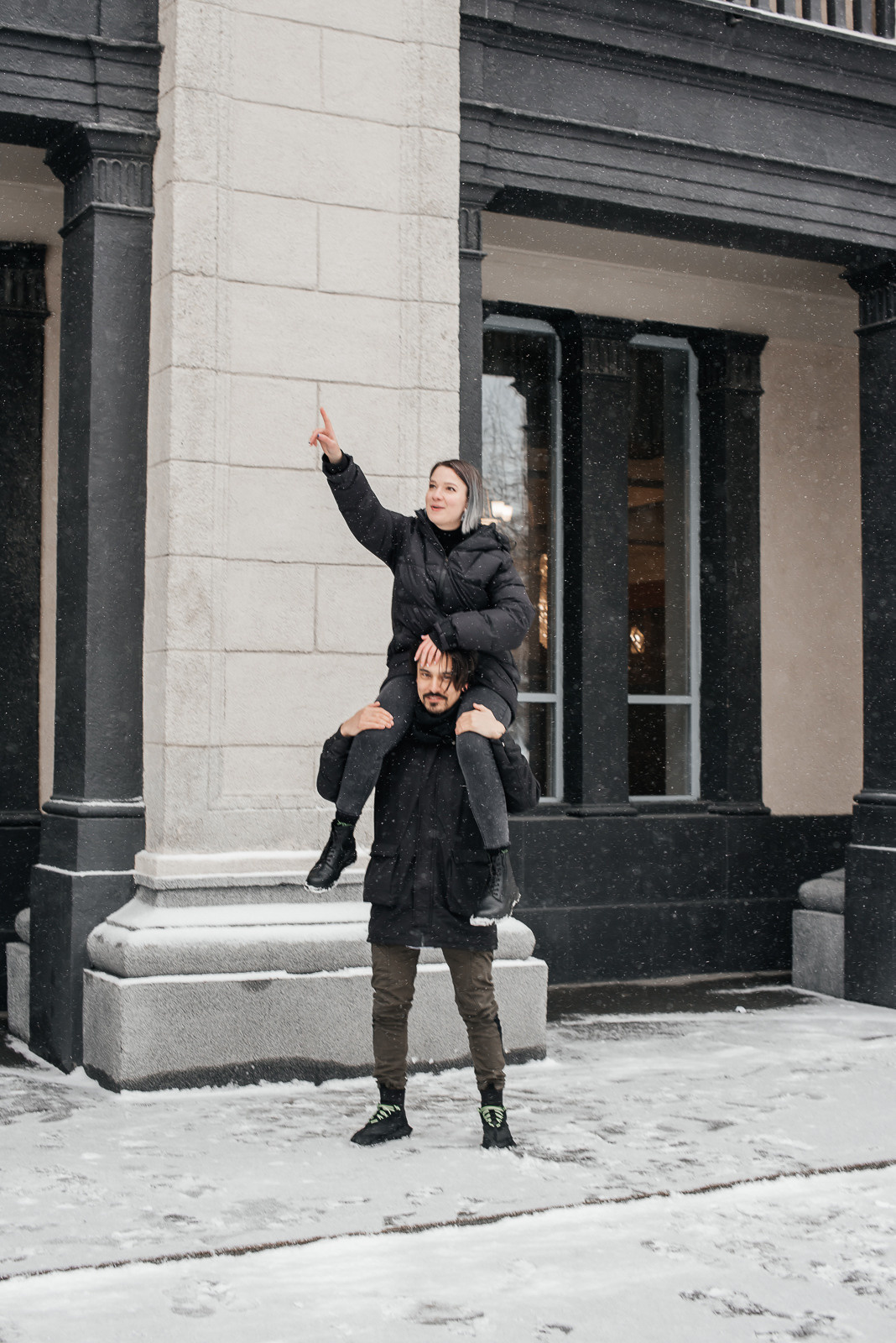 парень держит девушку на плечах на фоне здания