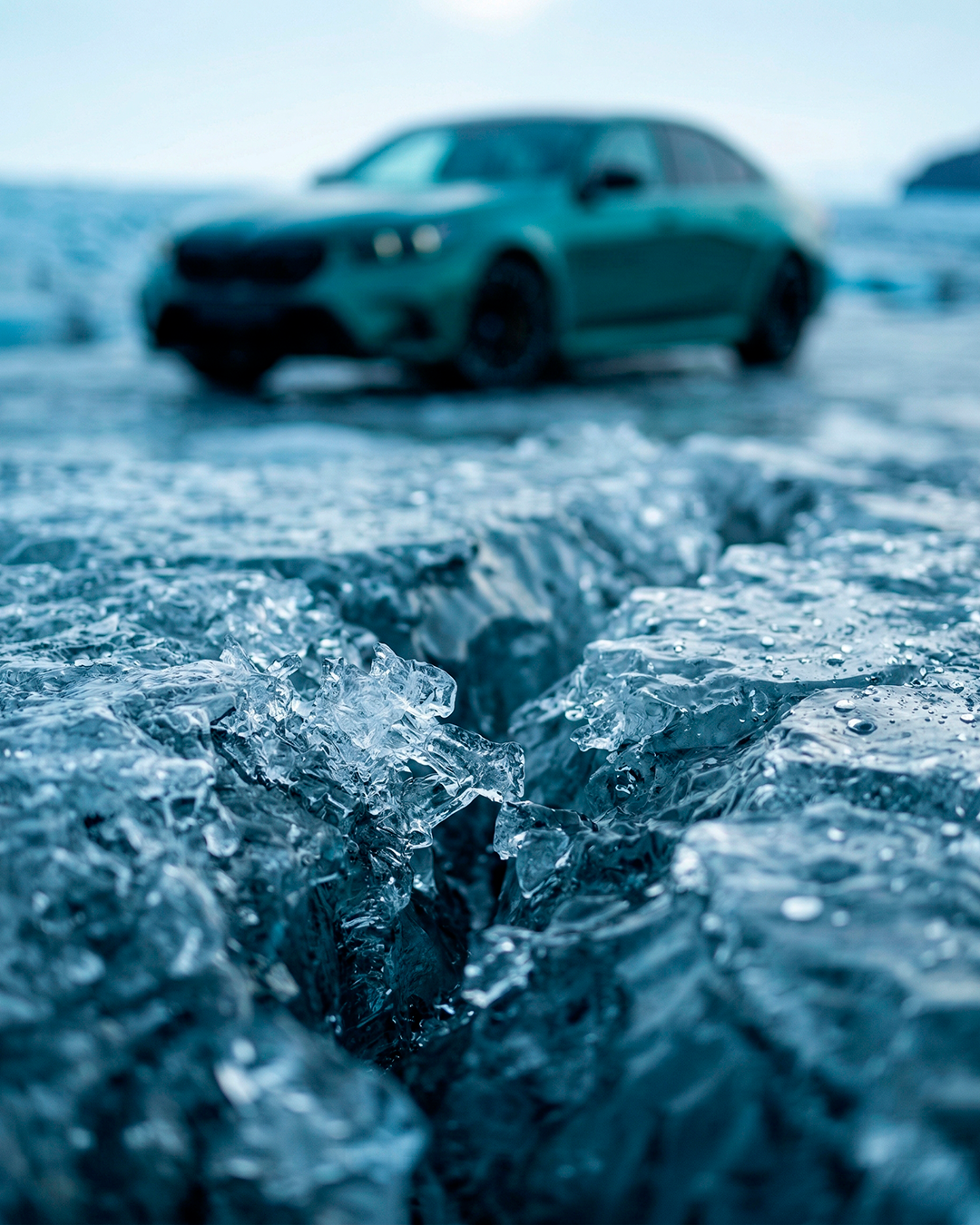 Макро съёмка трещины в прозрачном льду с каплями воды на переднем плане BMW M5 размыта в боке на заднем плане CGI визуализация