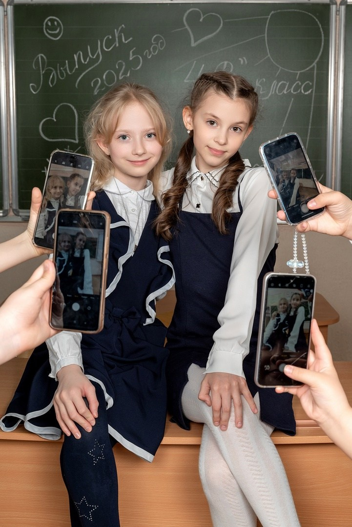 Девочки делают селфи сидя на парте под пристальным взором камер объектива.