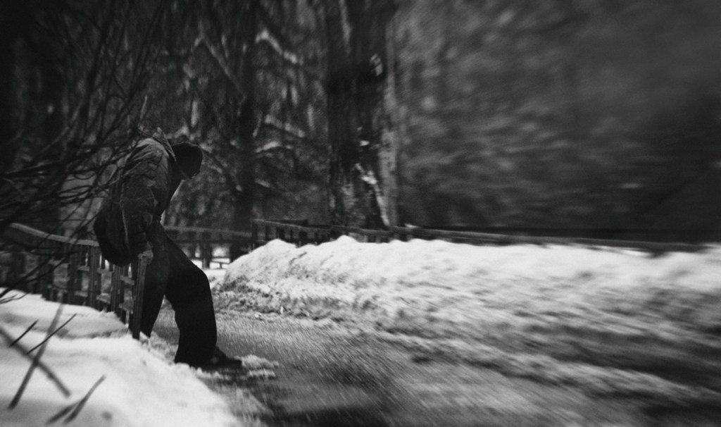 Человек идущий по заснеженной улице с эффектом размытия движения, зимний городской пейзаж, деревья на фоне