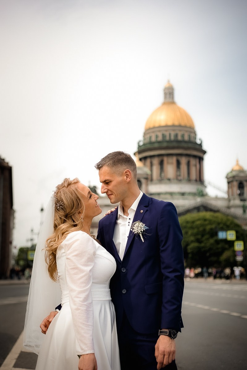 Жених и невеста смотрят друг на друга на фоне Исаакиевского собора в Санкт-Петербурге. Вертикальный поясной кадр.