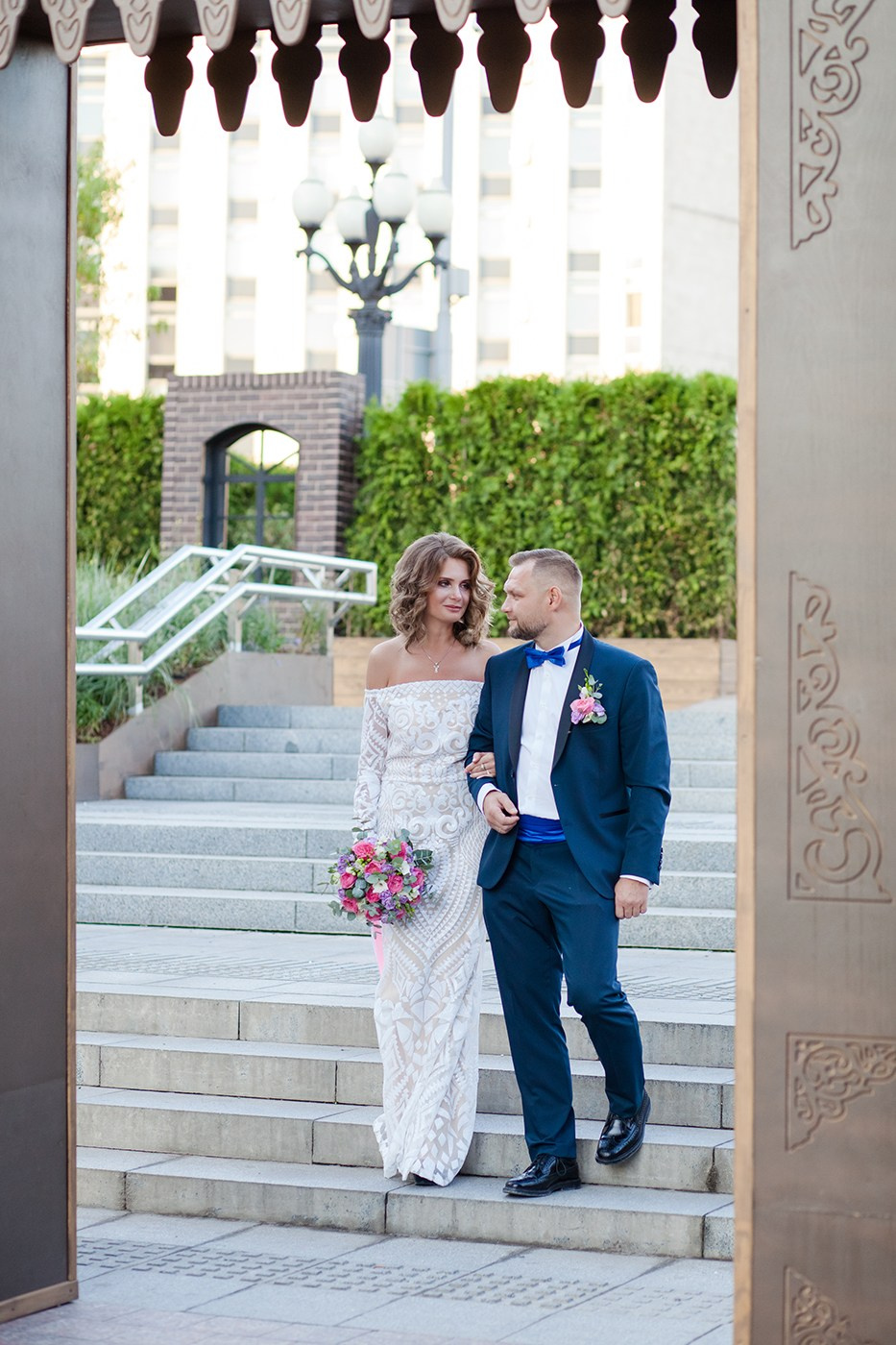 Жених синем костюме и невеста в белом платье спускается по лестнице