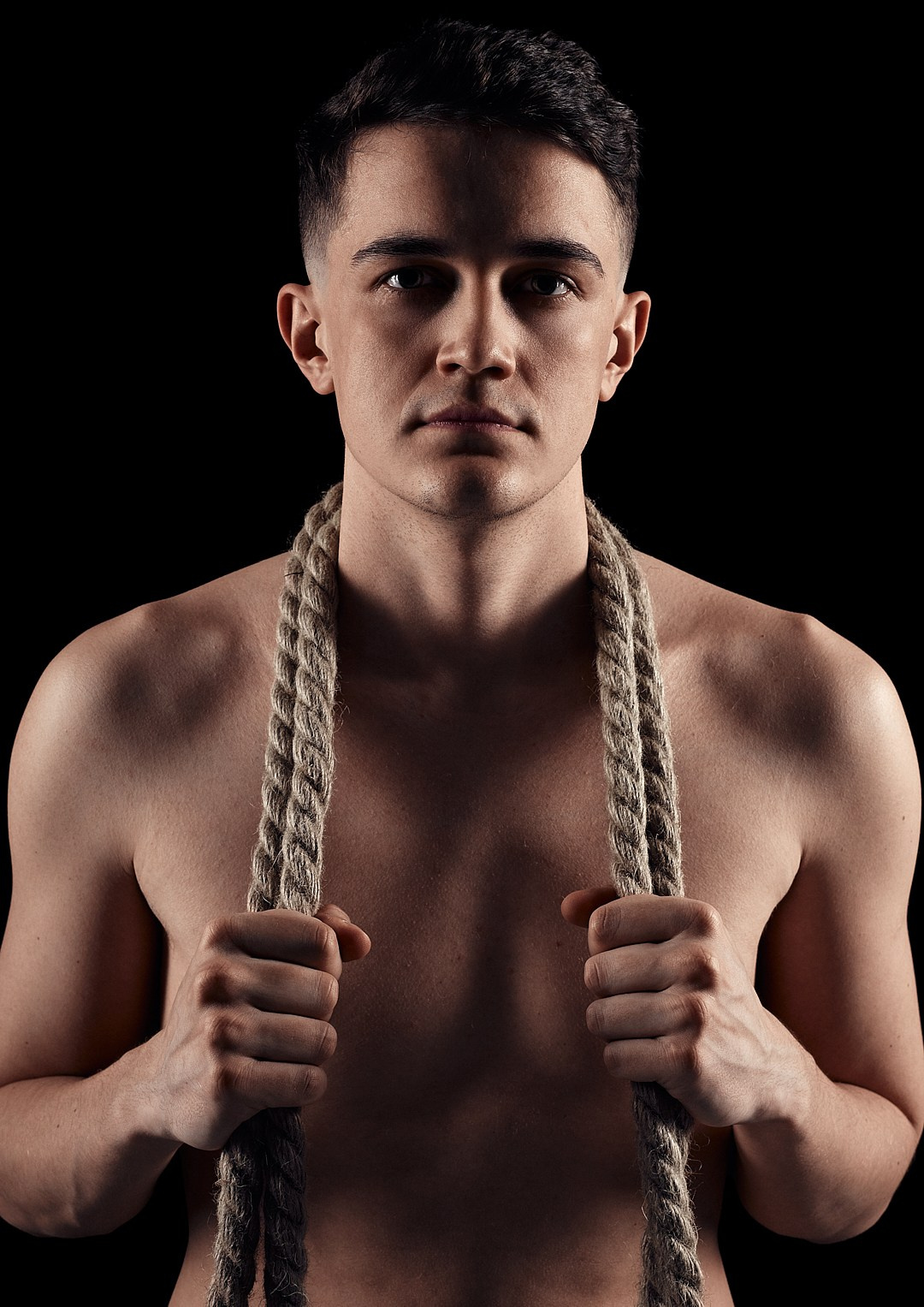 Мужчина с голым торсом сильным хватом держит веревку, мужской портрет на черном фоне Казань