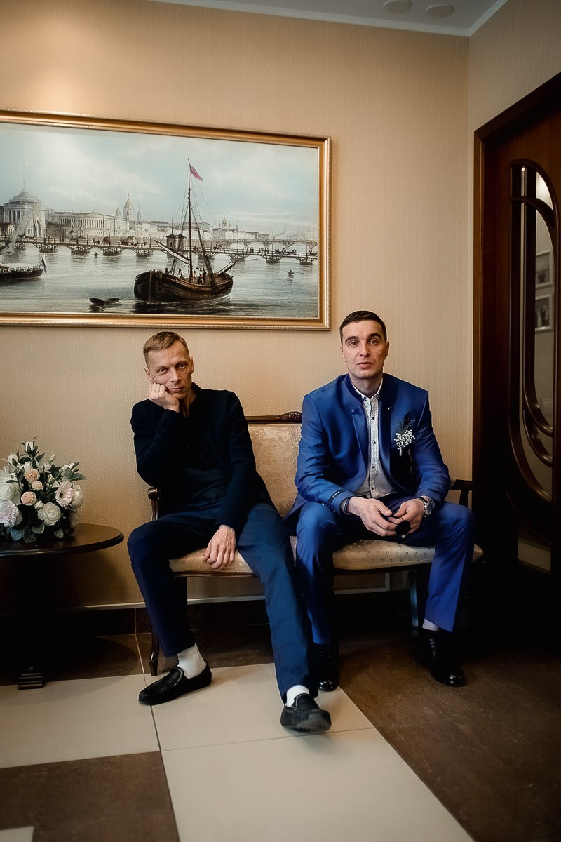 Гости сидят на диване в здании в ЗАГСе на Васильевском острове в Санкт-Петербурге. Вертикальный поясной кадр.