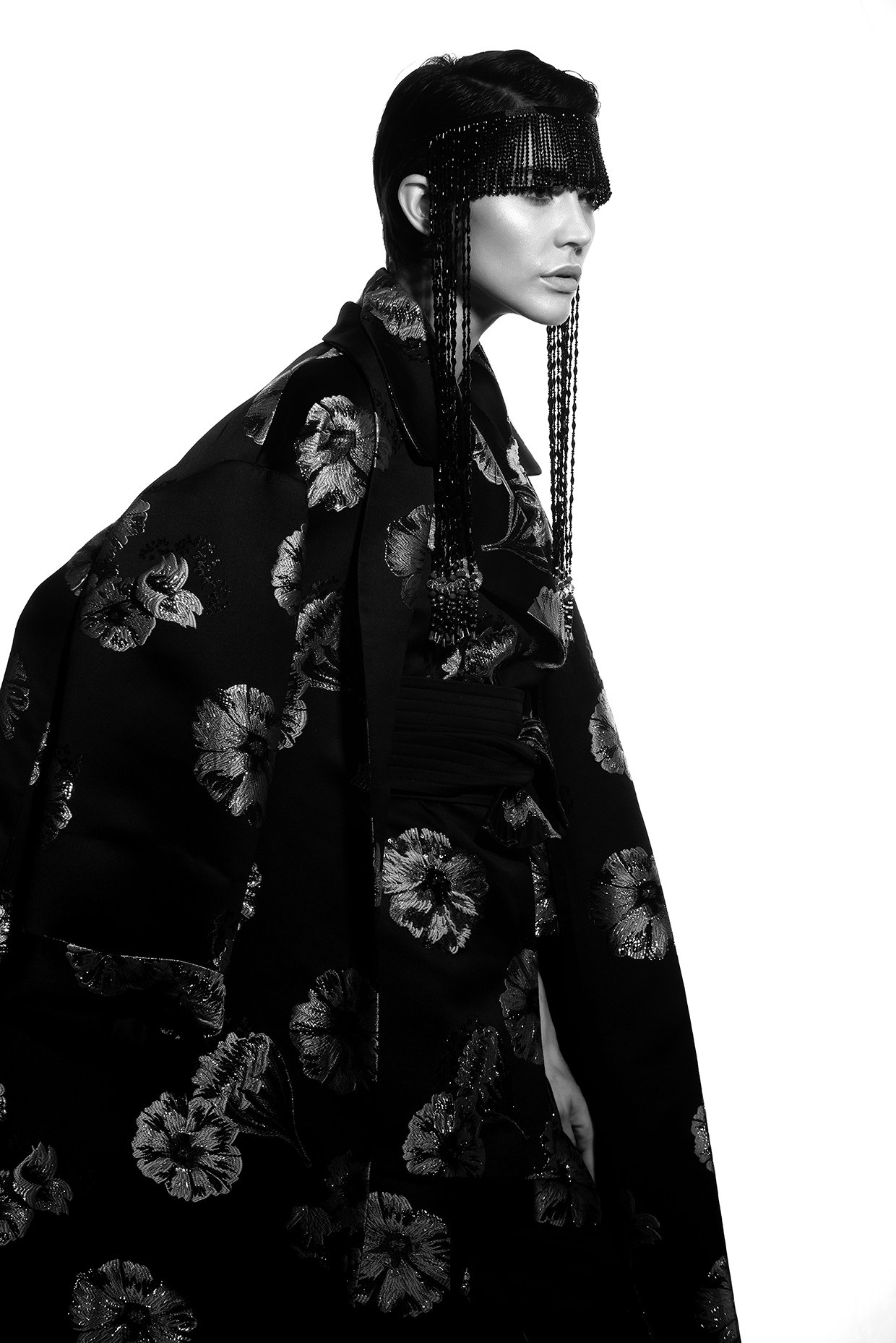 Студийная fashion-съёмка: модель в тёмном жакете с цветочным жаккардом и маской из длинной бахромы.