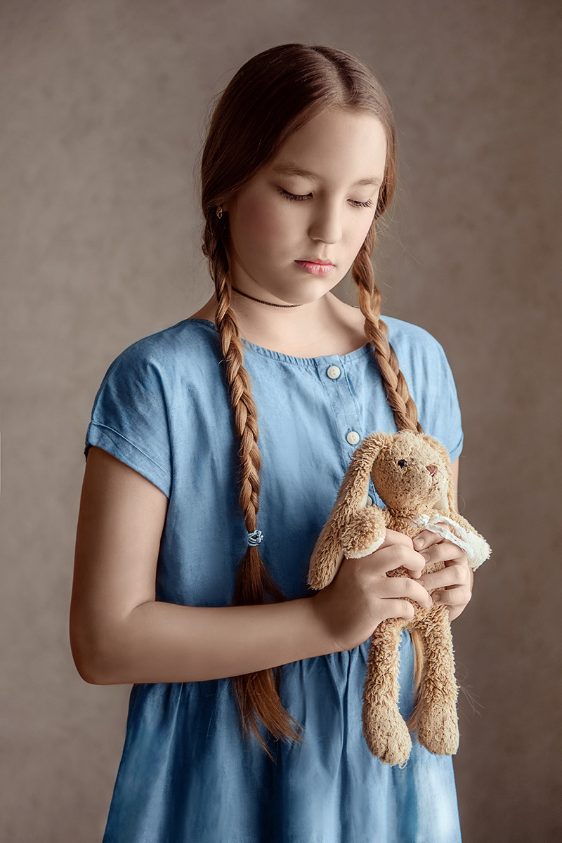 Школьница с косичками смотрит на игрушечного медвежонка в руках.