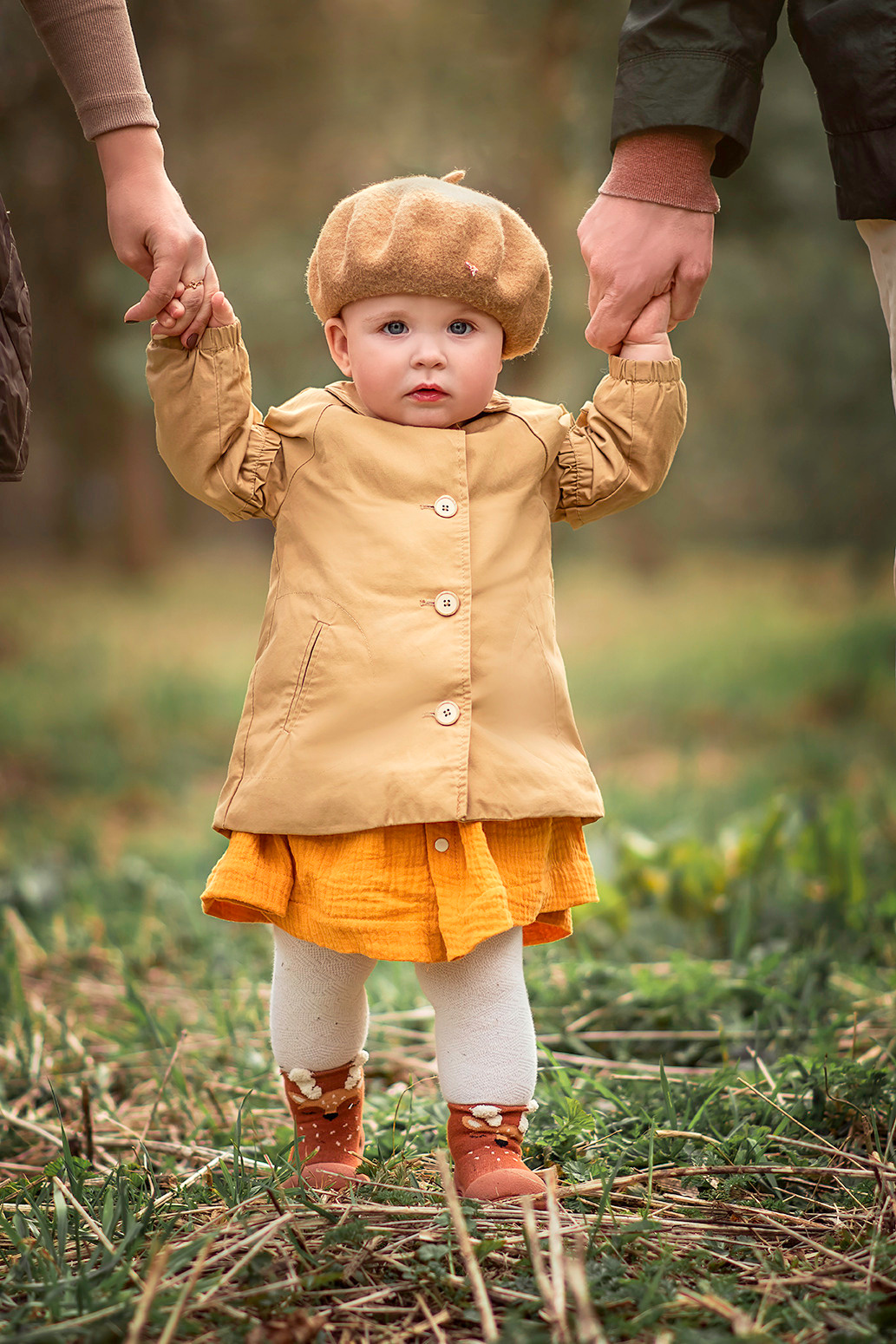 Маленький ребенок учиться ходить, держась за руки мамы и папы.