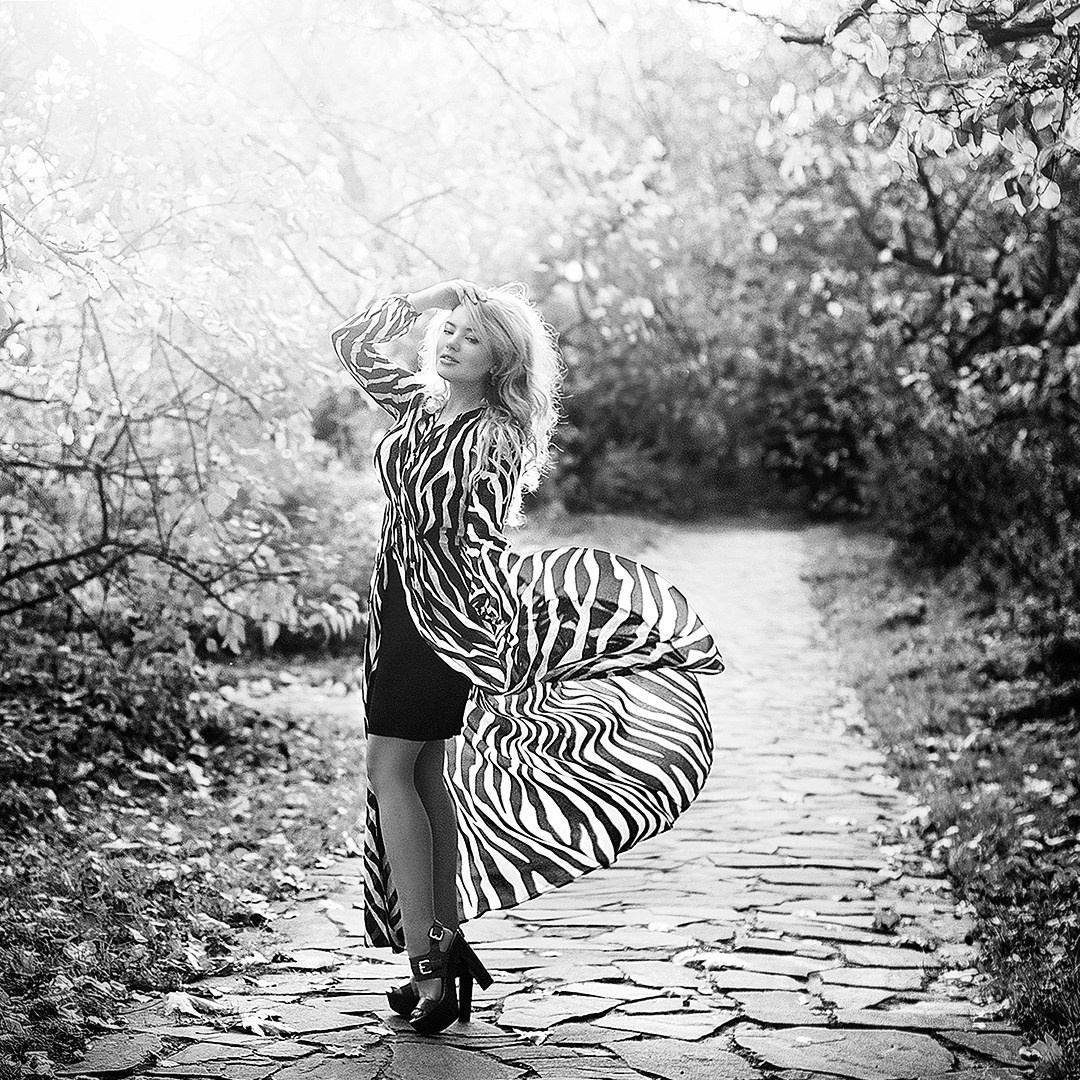 Улыбчивая блондинка в платье расцветки зебры стоит в солнечных лучах 