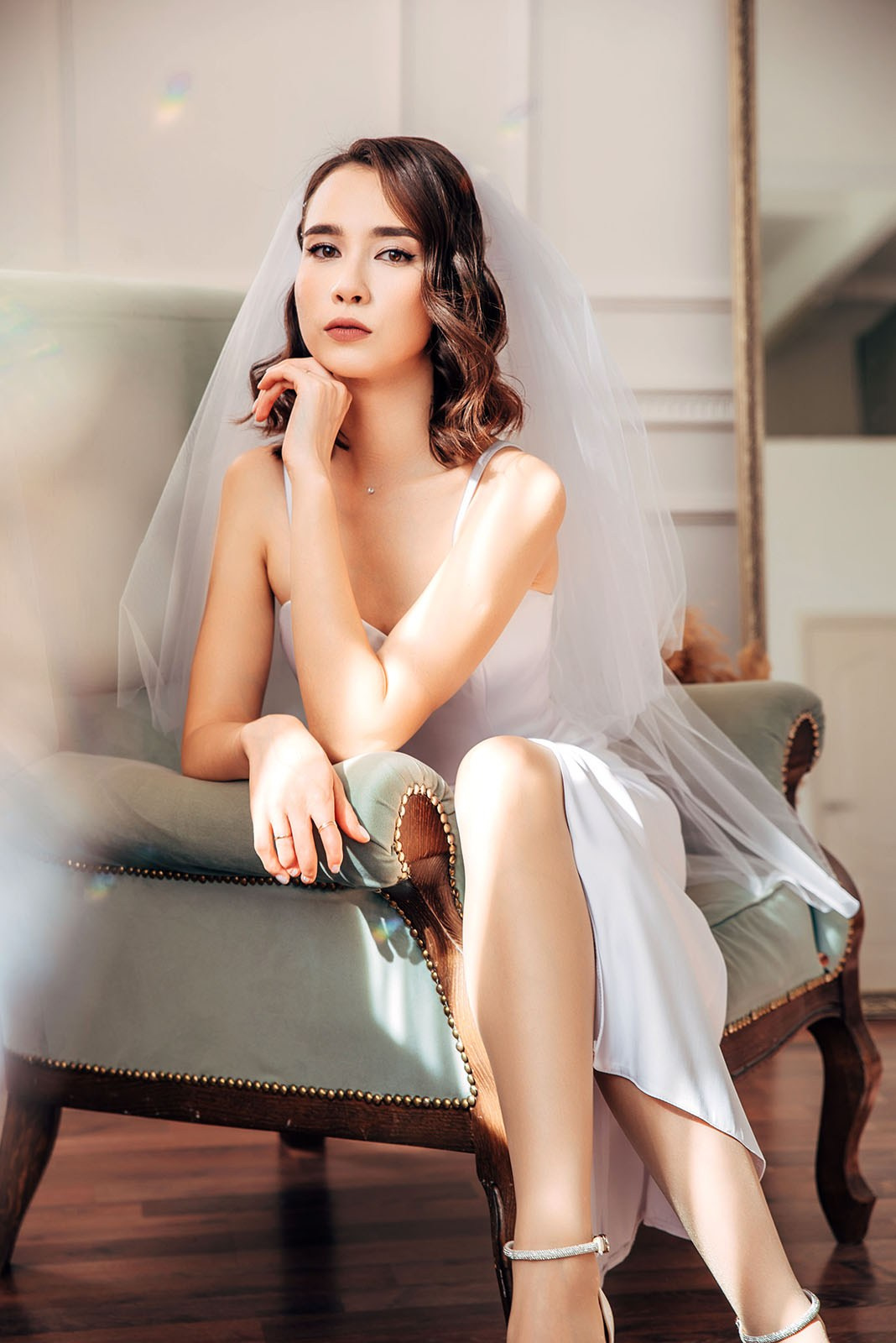 Невеста в белом платье сидит в кресле фотостудии