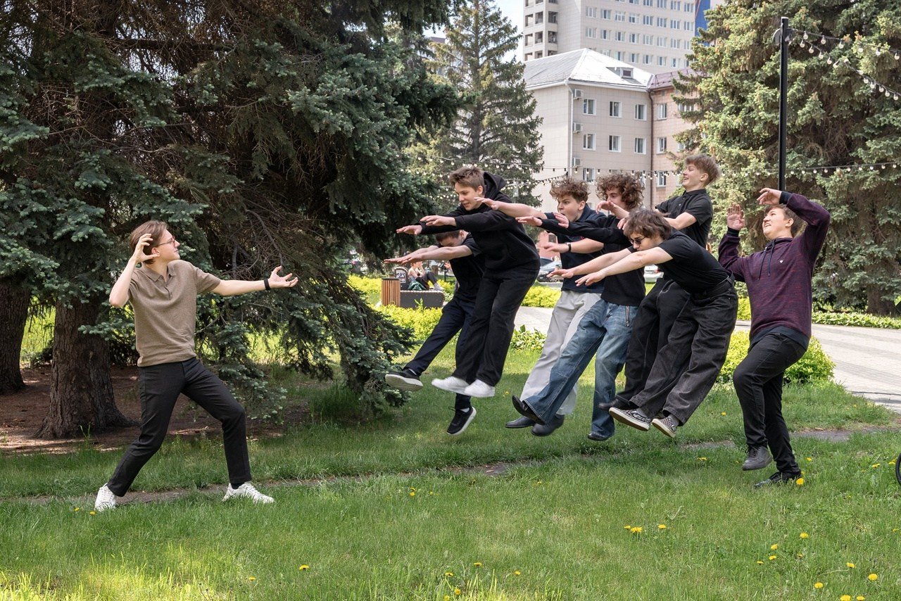 Школьники игриво бесятся прыгают скачут и позируют фотографу на лужайке.