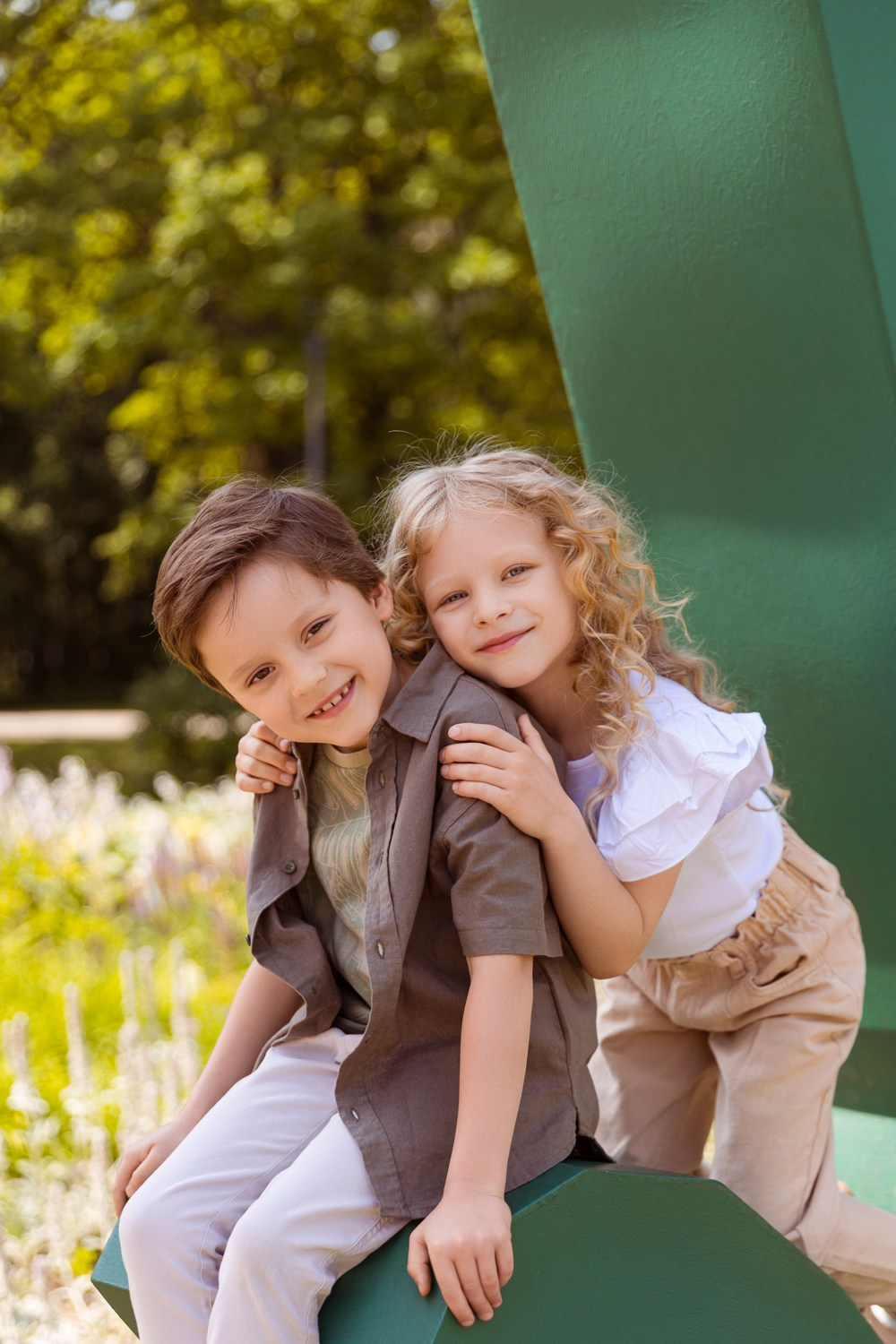 Мальчик и девочка сидят между пальцами уличной инсталляции в виде руки.