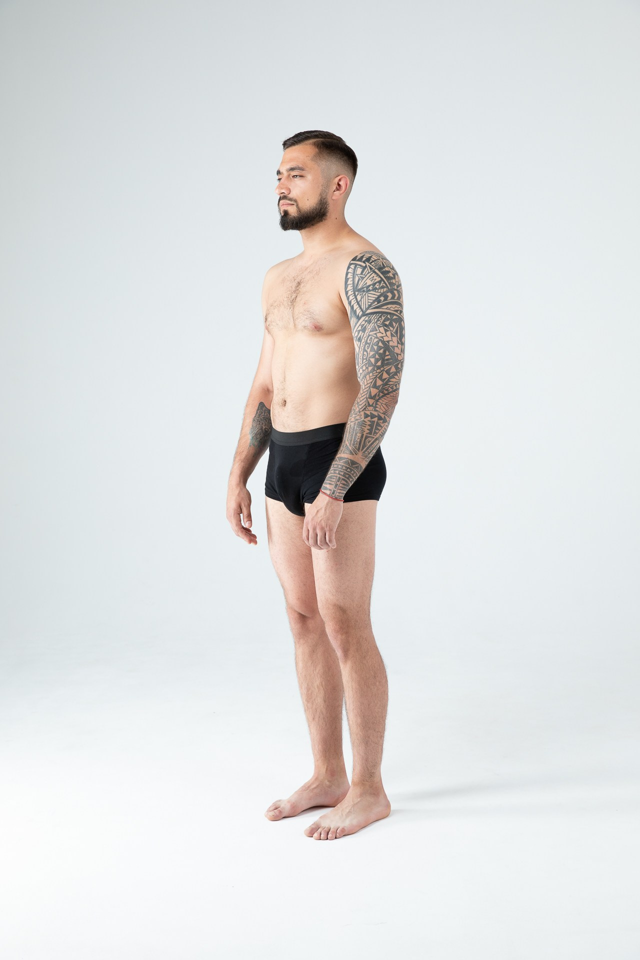 Мужчина модель с бородой с татуировками в черных трусах