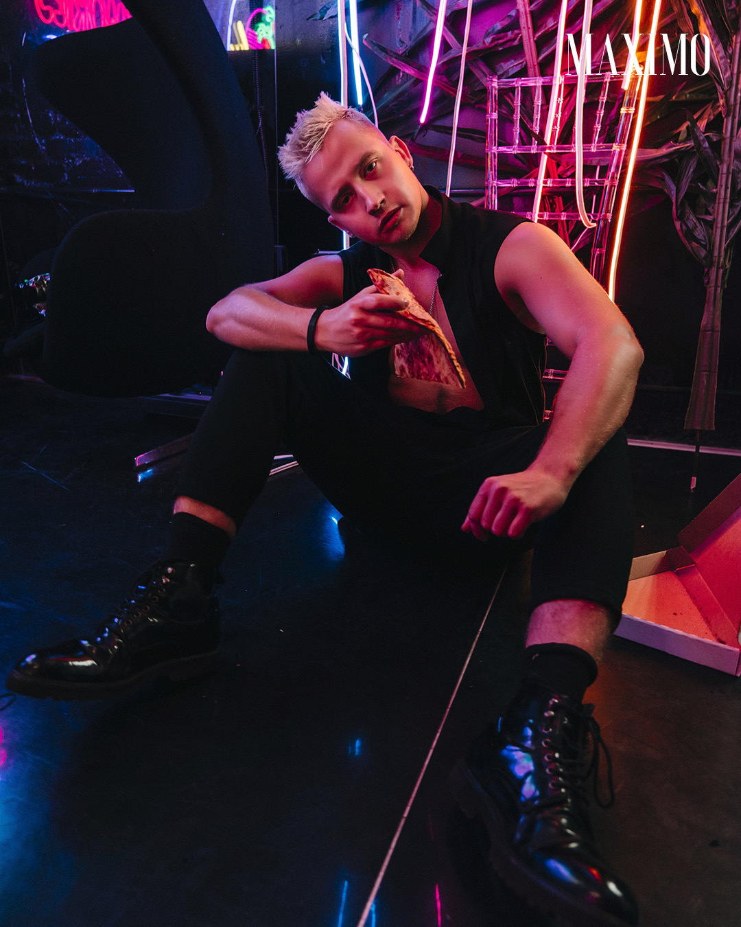 Мужчина блондин на фоне неонового света ест пиццу.