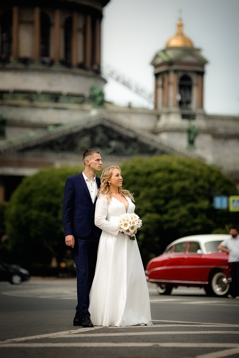 Жених и невеста смотрят в даль на фоне Исаакиевского собора в Санкт-Петербурге. Вертикальный ростовой кадр.