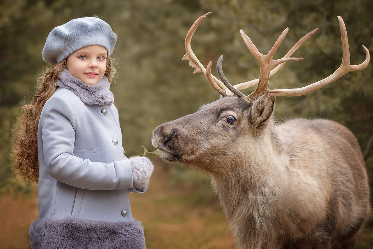 Девочка фотографируется с оленем в лесу осенью.