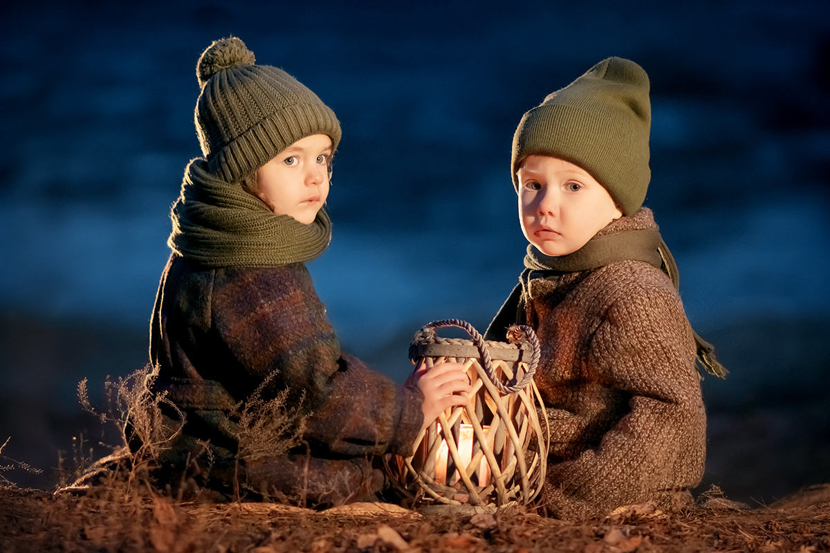 Два мальчика сидят на берегу вечером с фонариком.