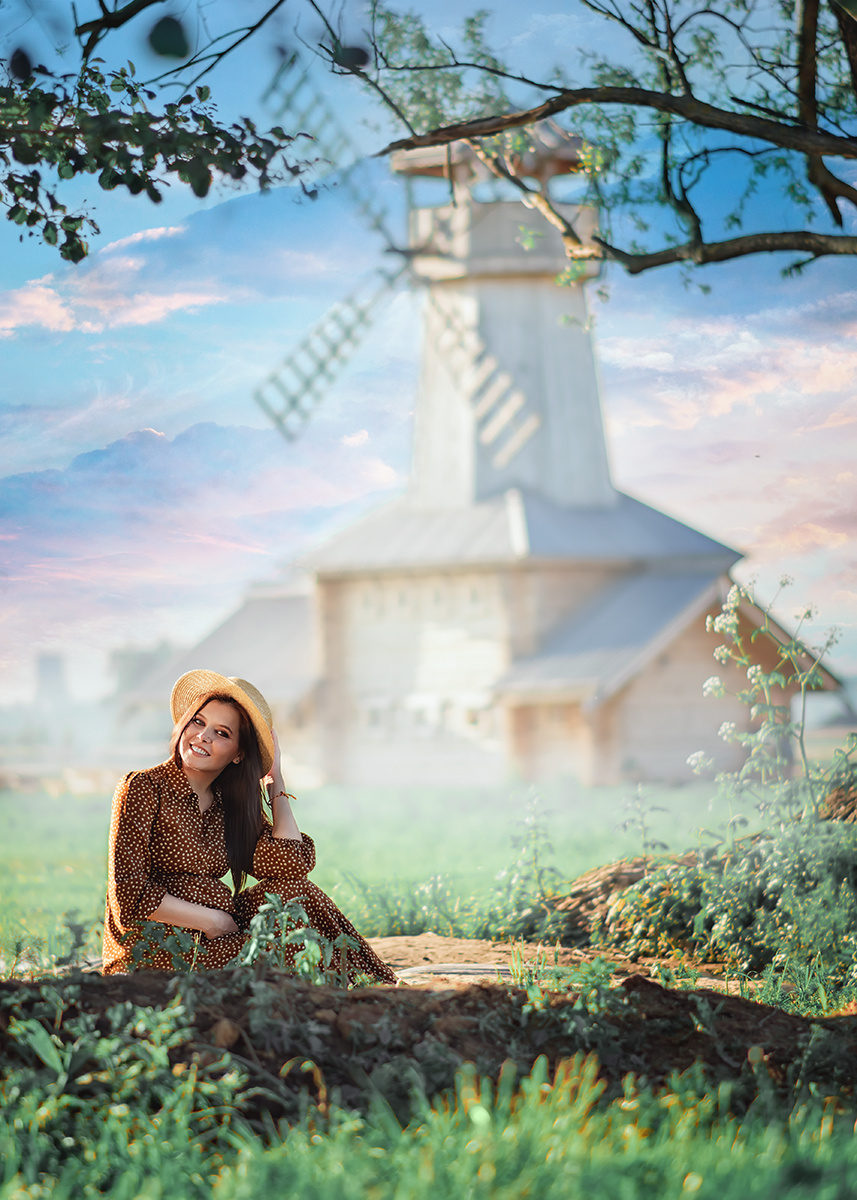 Беременная девушка фотографируется на фоне мельницы.