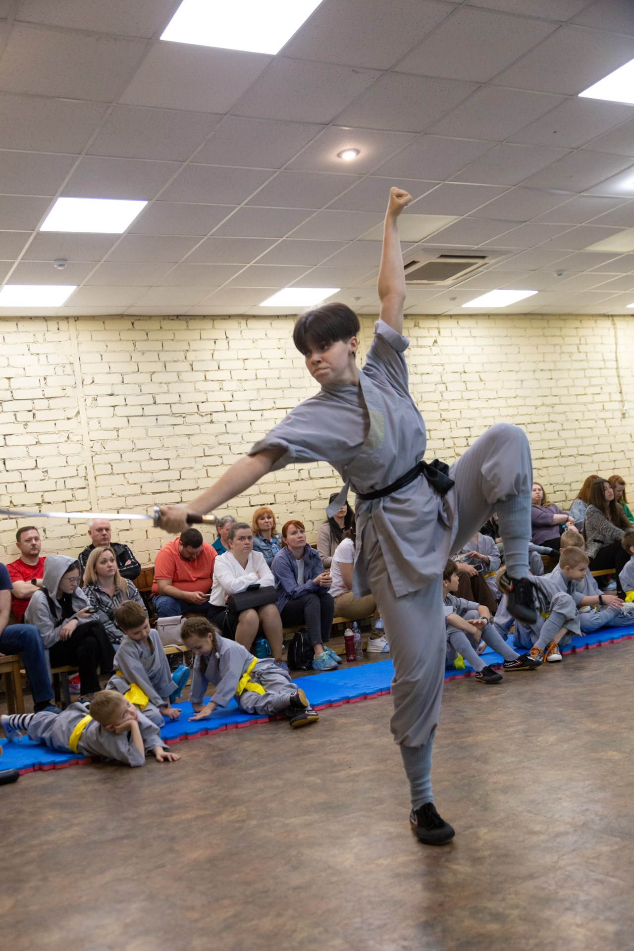 Девушка с широким мечом дао в высокой стойке ушу на одной ноге. Ушу для детей.