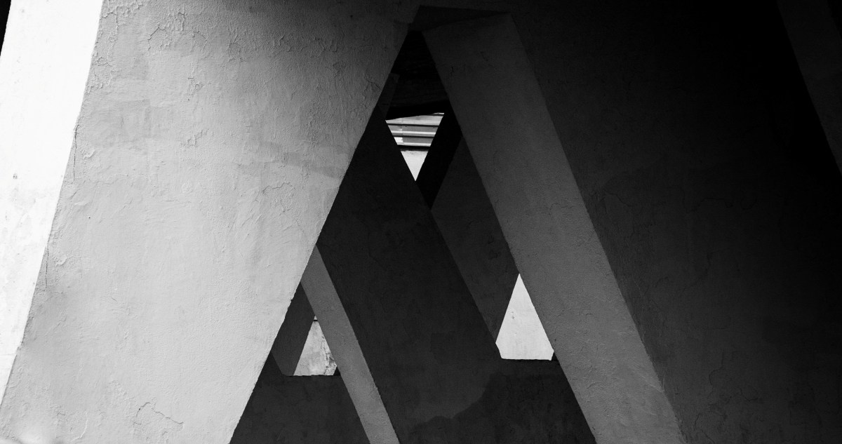 Черно-белая архитектурная фотография: абстрактная геометрия бетонных конструкций моста или эстакады, сходящиеся балки создают треугольные проемы, в центре узкая щель с ярким светом, контраст света и тени, минимализм, Вадим Топорёнок, Манифест теней, городская фотография, архитектура Москвы.