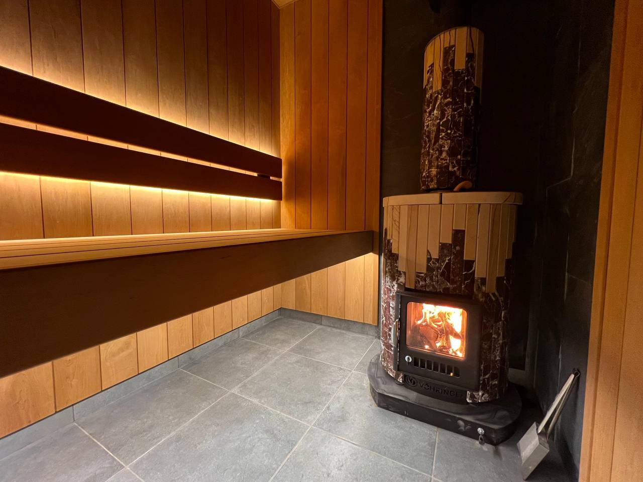 Уютная парная в Колтушах: внутренняя топка, печь в редкой облицовке, термоольха и тёплая линейная подсветка. SaunaTopMasters
