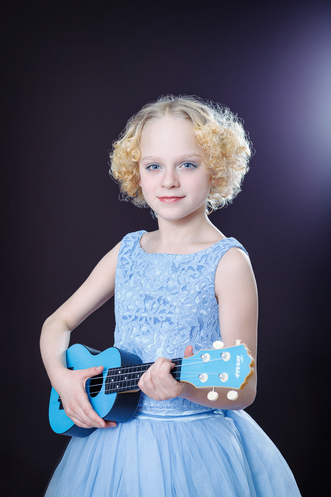 Девочка в голубом платье держит в руках укулеле