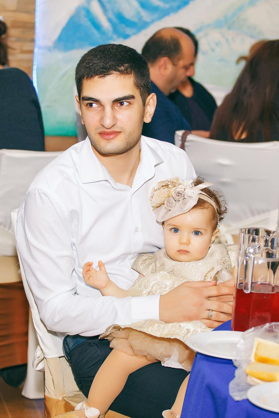 Молодой человек держит на руках малышку в красивом платье