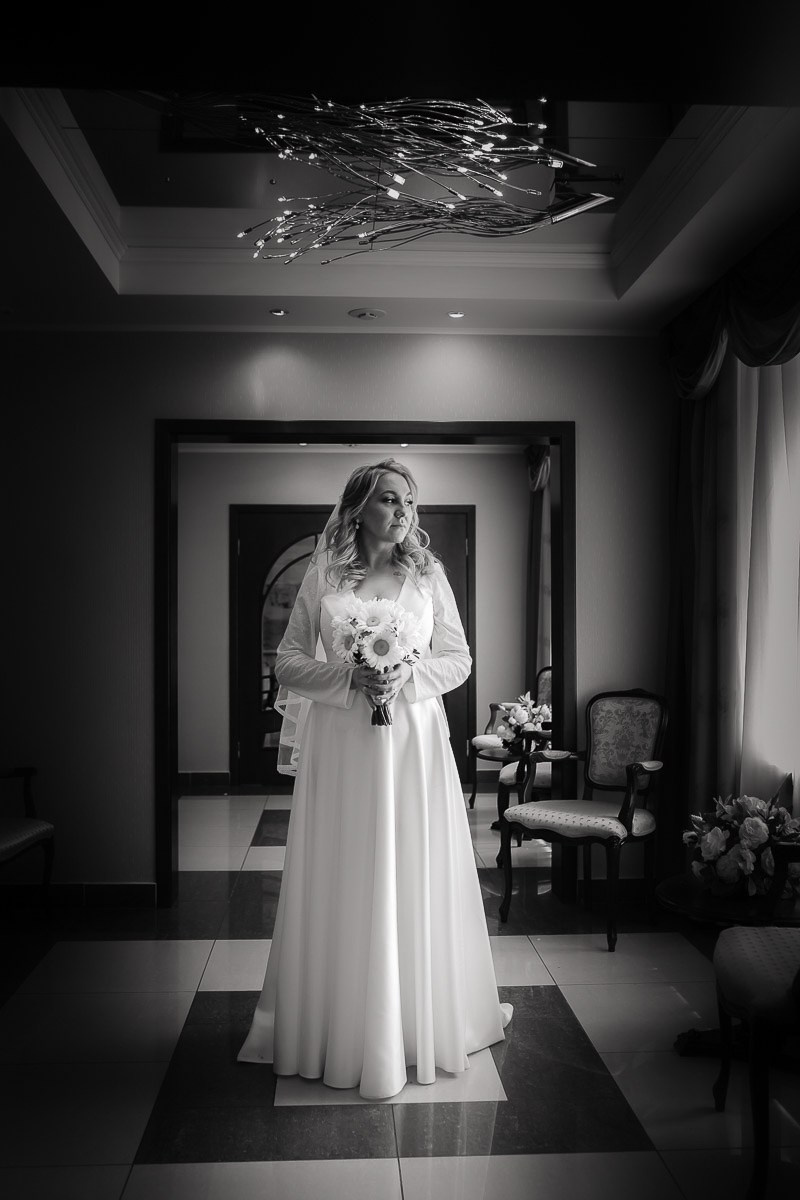 Невеста смотрит в окно после регистрации брака в ЗАГСе на Васильевском острове в Санкт-Петербурге.  Вертикальный чёрно-белый ростовой кадр.