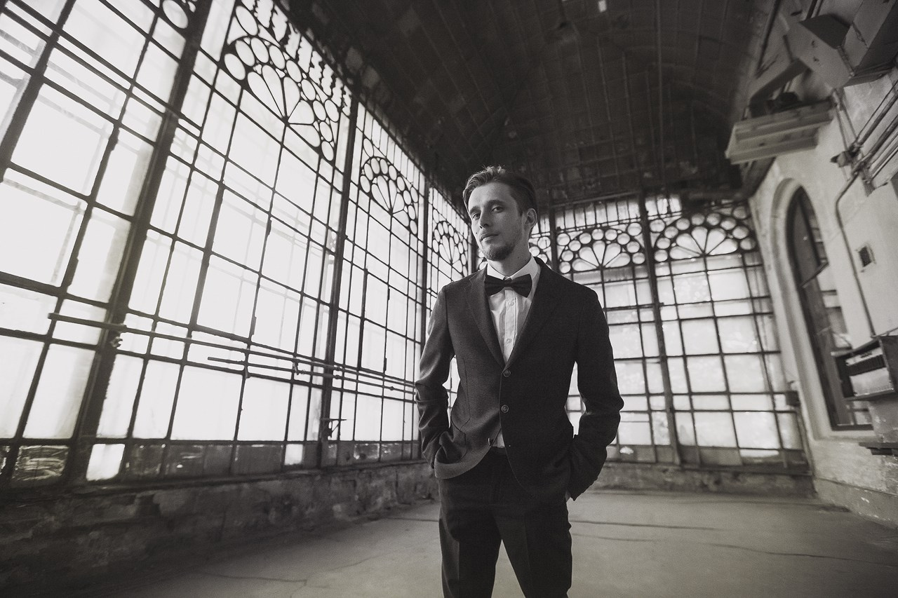 стильный портрет жениха одетого в костюм и бабочку на фоне оранжереи 