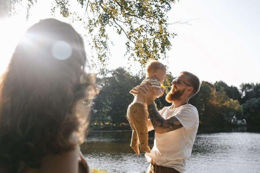 Мужчина в белой футболке поднимает малыша, а мама смотрит на них