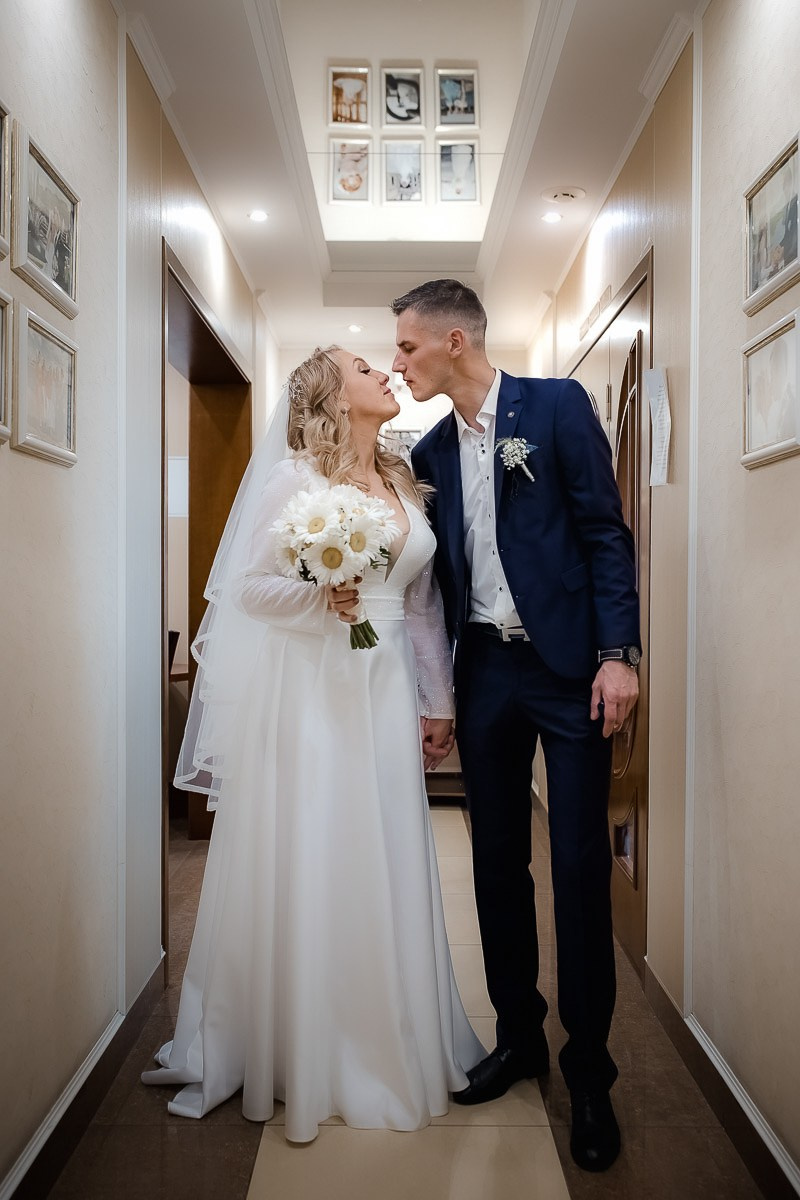 Жених и невеста целуются в коридоре после регистрации брака в ЗАГСе на Васильевском острове в Санкт-Петербурге.  Вертикальный ростовой кадр.