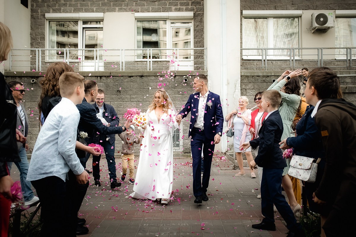 Гости встречают молодожёнов на выходе из ЗАГСа на Васильевском острове в Санкт-Петербурге. Горизонтальный  ростовой кадр.