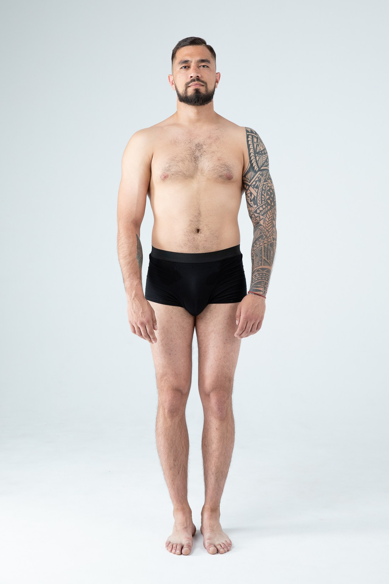 Мужчина модель с бородой с татуировками в черных трусах