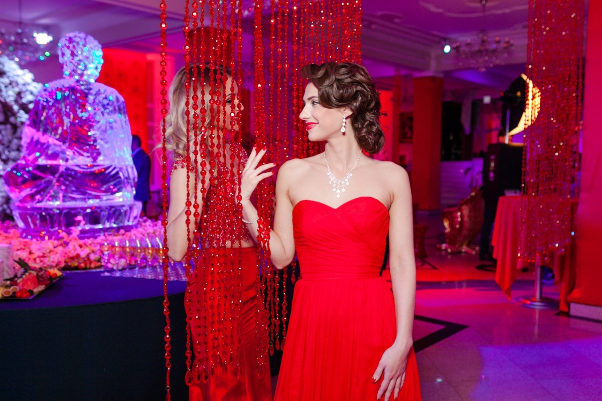 Две девушки в красных платьях смотрит друг на друга через красную занавеску