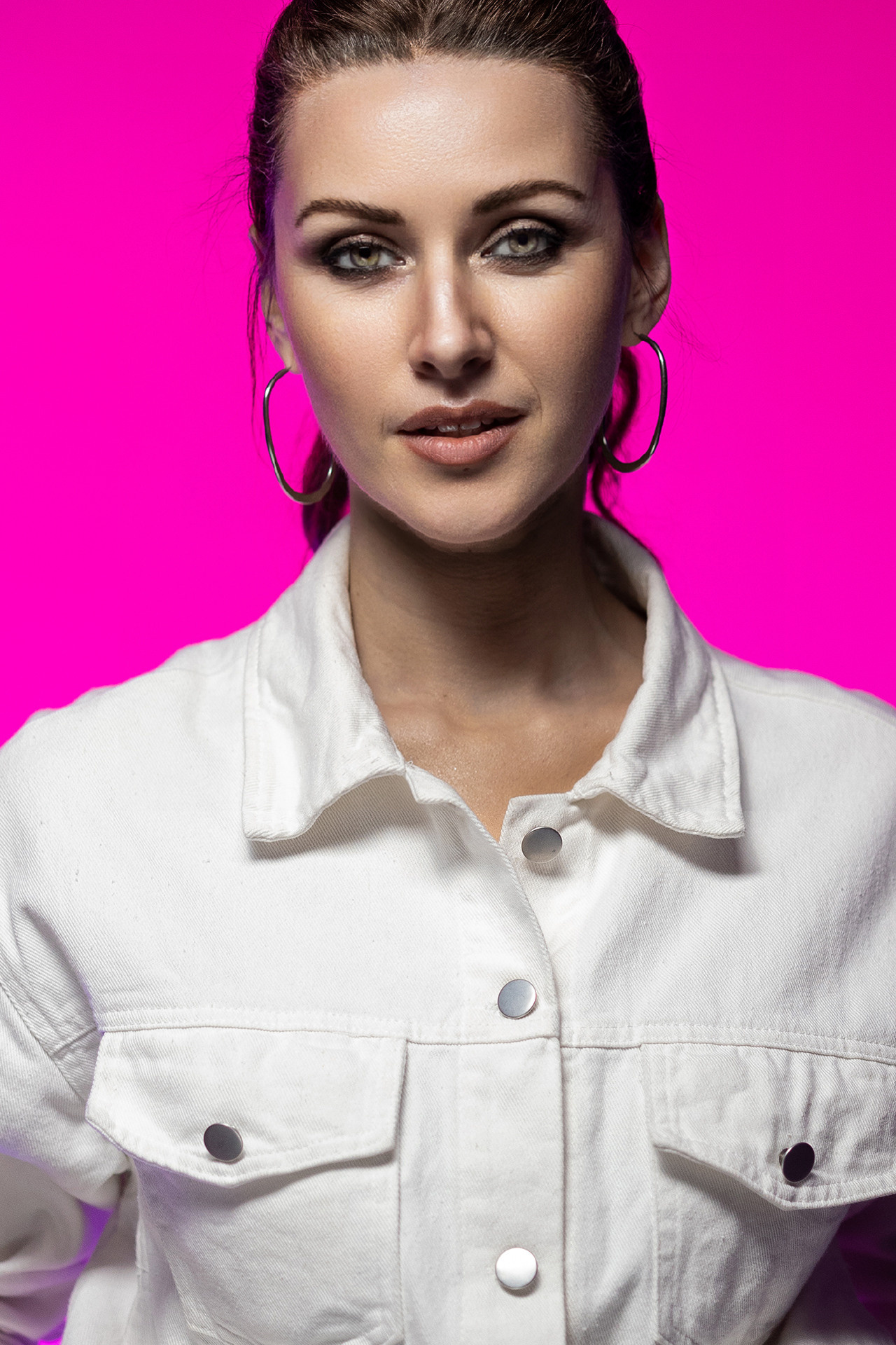 Девушка модельной внешности в белой джинсовой куртке на розовом фоне