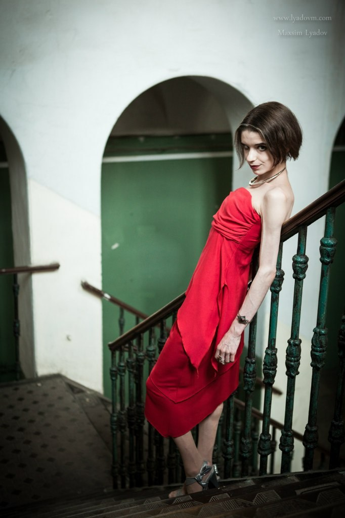Модель в красном платье на лестнице в старом здании, так проходит художественная фотосессия