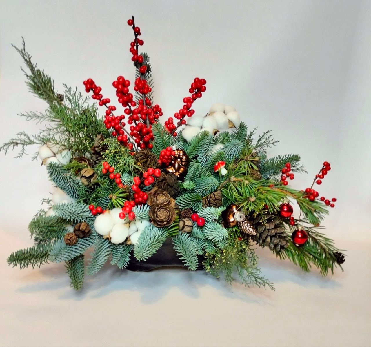 Композиция в керамическом кашпо из натуральной хвои с ярко-красным илексом в современной флористике. По желанию заказчика добавлен ярко-красный илекс, хлопок, натуральный декор (шишки)